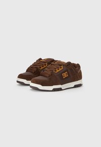 Brown sneakers with a mix of suede and synthetic materials. Features a white sole, brown laces, and a prominent DC logo in gold.