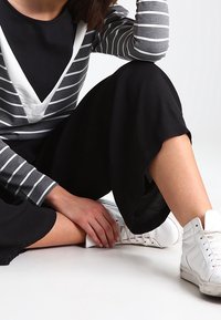 Schwarze Culottes mit lockerem Schnitt, kombiniert mit einem grau-weiß gestreiften Langarmshirt mit V-Ausschnitt. Weiße Sneakers inklusive.