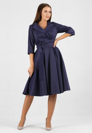 Marineblaues Wickelkleid mit Dreiviertelärmeln und gebundenem Taillenband. Ausgestellter Rock und glatte Textur. Ein subtiler Glanz verleiht ein elegantes Aussehen.