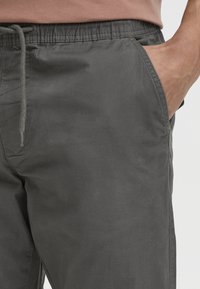 Gray lightweight pants with an elastic waistband, drawstring detail, and side pockets. Fabric texture appears soft and smooth.