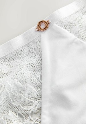 Bílé spodní prádlo kombinující jemnou krajku a hladkou látku, zdobené kulatou sponou v růžovozlaté barvě.