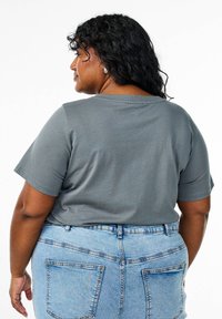 T-shirt grigio in cotone con maniche corte. Indossato con jeans a vita alta di colore blu chiaro, con tasche posteriori e cuciture visibili.