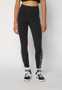 Black leggings with a high waist, featuring white zigzag stripes down the sides. Paired with black and white sneakers and white socks.