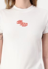 Hvid bomulds T-shirt med et rødt grafisk logo, der står "KARL LAGERFELD JEANS," med en tætsiddende silhuet og korte ærmer.