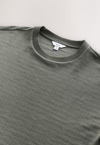 Donkergroene trui met ronde hals, voorzien van een gestructureerd patroon, geribbelde halslijn en zichtbare label. Gemaakt van zacht, gemengd materiaal.