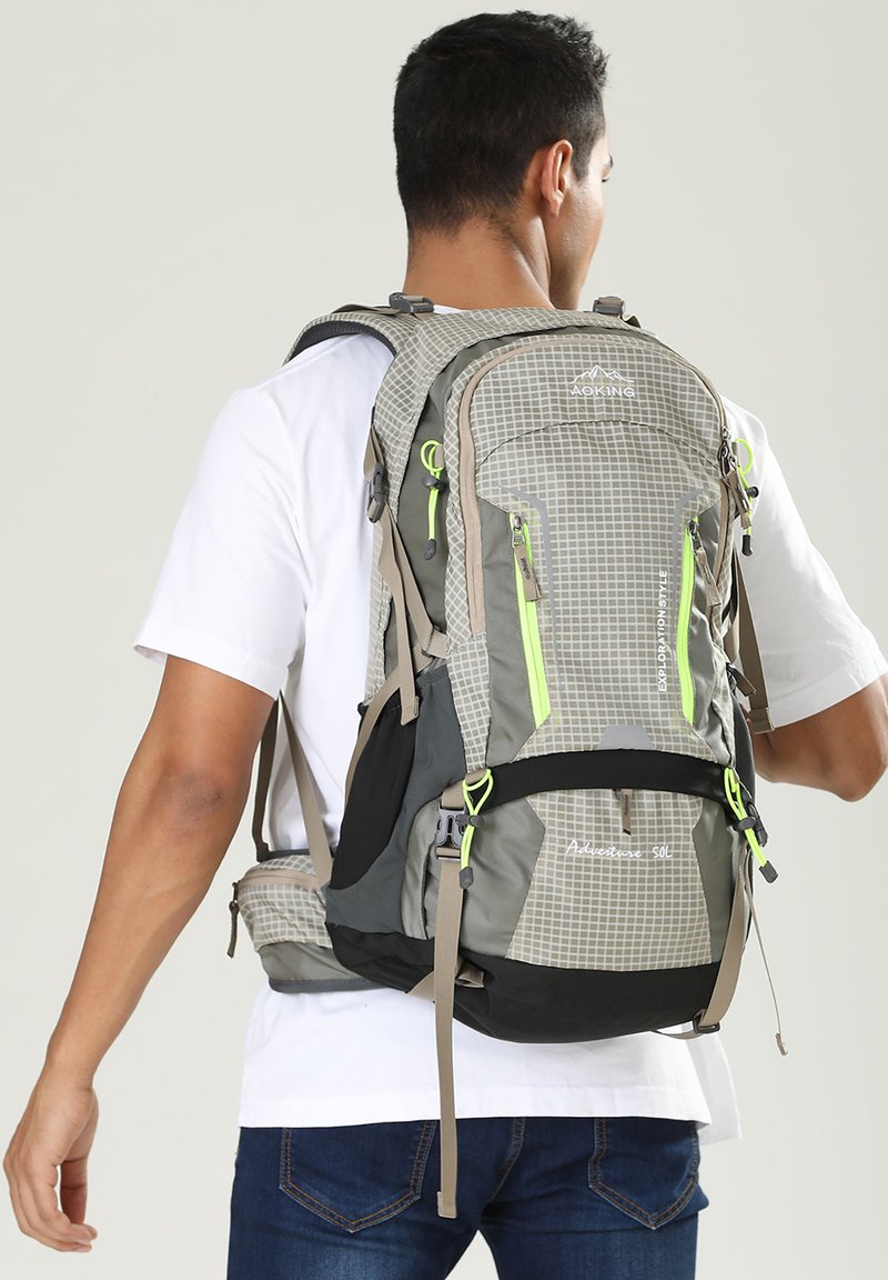 Sac à dos gris et noir avec un motif à carreaux, accents vert fluo, plusieurs zips, bretelles rembourrées et une ceinture de hanche pour la stabilité.