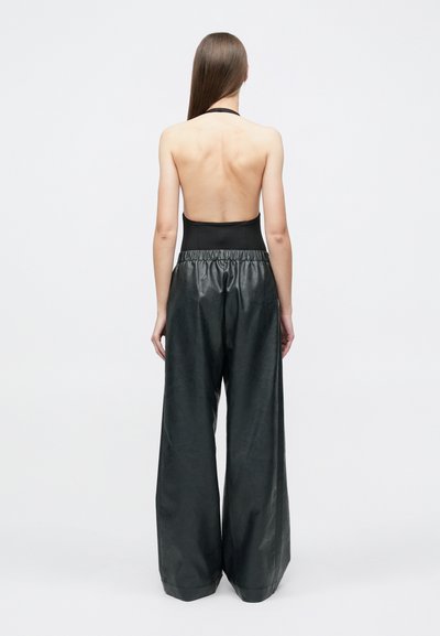 Čierny top na vystrihnutie za krk s odhalenými chrbtom; doplnený o široké lesklé čierne kožené nohavice s pružným pásom a hladkým povrchom.