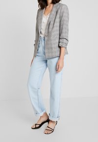 Grå rutmönstrad kavaj med avslappnad passform, kombinerad med högmidjade ljusblå jeans och svarta sandaletter med remmar. Slät tyg, strukturerad design.