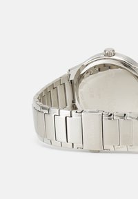 Reloj de acero inoxidable plateado con un acabado pulido y cepillado, que cuenta con una pulsera de eslabones de metal y una caja redonda simple con una corona.