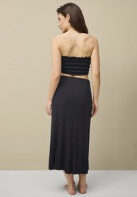 Zwarte two-piece outfit met een aansluitende smocked bandeau-top en een lange, vloeiende rok van zacht, lichtgewicht materiaal.