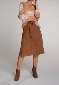 Pull tricoté beige et marron, avec un col en V et des manches trois-quarts. Jupe en daim marron avec taille à nouer, boutonnée à l'avant, et coupe évasée.