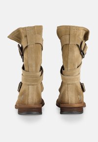 Botas de tobillo de ante en marrón claro con un puño doblado, dos correas ajustables con hebillas y un tacón bajo de madera. Vista trasera mostrando los detalles de costura.
