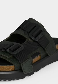 Σκούρο πράσινο σανδάλι Birkenstock με δύο ρυθμιζόμενους μαύρους ιμάντες και φαρδιά φιάλη φελλού σε μαύρη σόλα.