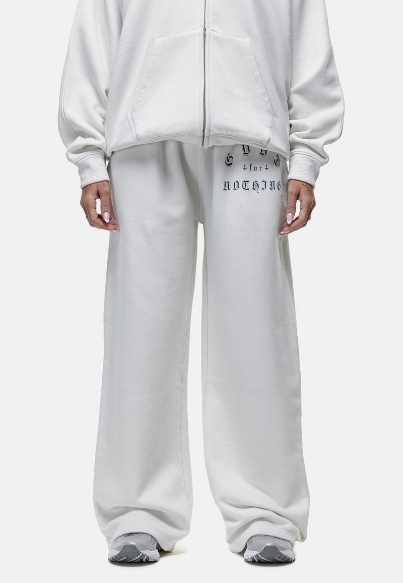 Witte hoodie met een rits aan de voorkant en kangoeroezakken, gecombineerd met witte sweatpants met een gedrukt tekstdetail op de linker bovenbeen.