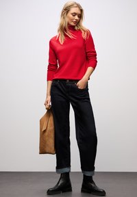 Maglione a collo alto rosso, jeans a gamba larga blu scuro con orli arrotolati, stivaletti neri alla caviglia e borsa a tracolla in suede beige. Texture morbida e vestibilità casual.