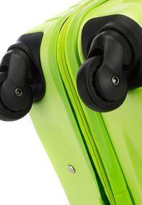 Valigia rigida verde con superficie testurizzata, doppie ruote nere e una cerniera verde coordinata. Presenta un dettaglio con bottone a pressione metallico.