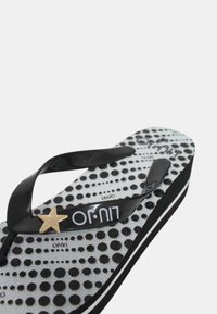 Infradito neri con una suola bianca testurizzata caratterizzata da pois neri, una cinghia nera e un accento decorativo a forma di stella dorata.