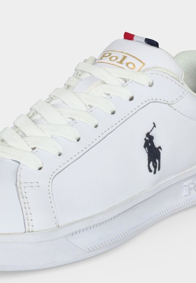 Biały skórzany sneaker z białymi sznurowadłami, czarne wyszywane logo marki Polo po boku oraz czerwono-biało-niebieskie detale na języku buta.