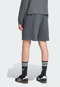 Šedé sportovní šortky s elastickým pasem, kombinované s černobílými pruhovanými ponožkami a černými teniskami. Zelené logo na šortkách.
