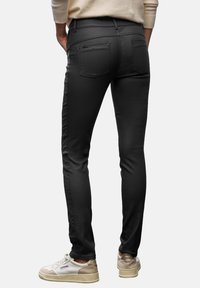 Jeans ajustados negros con una textura suave, detalles en el bolsillo trasero y un bolsillo con cremallera en la cadera derecha. Combinados con zapatillas blancas.