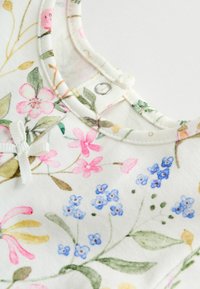 Kätketev riietus, millel on lilleline muster roosa, sinise ja rohelise värviga valgel taustal, nööbiga kinnitamine ja dekoratiivne lipsuelement.