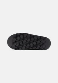 Black rubber shoe sole with a wave pattern and circular grip features. Smooth texture with a rounded heel and flat front edge.