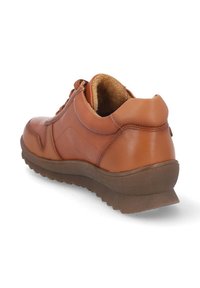 Zapatilla de cuero marrón con forma redondeada, suela de goma texturizada y un interior suave forrado de felpa. Presenta detalles cosidos en los laterales.