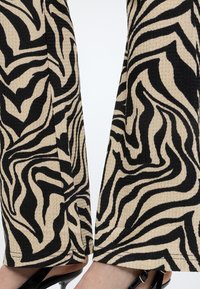 Primer plano de piernas con pantalones a rayas de cebra en beige y negro combinados con zapatos negros de tacón con tira trasera.