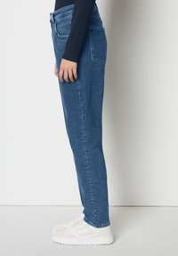 Blå denimbyxor med rak passform, med stitchade sömmar och medelhög midja, i kombination med vita sneakers.