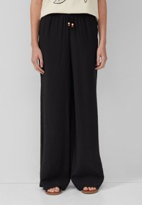 Schwarze weit geschnittene Hosen aus leichtem Material, mit einem elastischen Taillenbund und dekorativen Perlen, sowie einer glatten, strukturierten Oberfläche.
