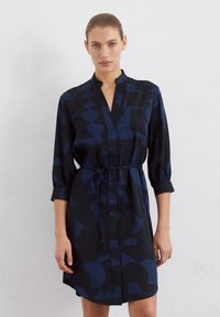 Robe bleu marine en tissu doux avec un motif géométrique, manches mi-longues, design sans col et taille nouée pour un ajustement réglable.