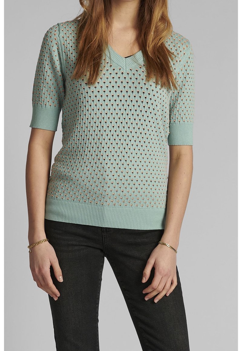 Pull vert menthe en maille avec un col en V, des manches courtes et de petites découpes en forme de losange partout. Les poignets et l'ourlet côtelés ajoutent de la texture.