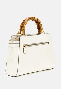Biała torebka o teksturowanej powierzchni, o wyraźnym kształcie, z akcentami z bambusowych uchwytów, złotymi detalami oraz zamykaną na zamek kieszenią z przodu.