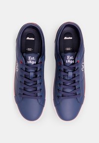 Sneakers blu navy con una toma in sintetico liscio, punta rotonda e design con lacci. Suola bianca con accenti rossi e marchio sulla linguetta.