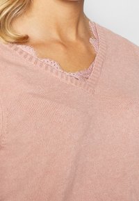 Helles rosa Strickpullover mit V-Ausschnitt und Spitze. Verfügt über gerippte Akzente am Hals und eine weiche, glatte Textur.