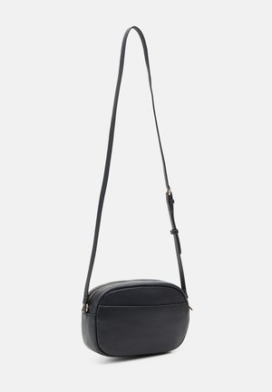 Sac bandoulière en cuir noir, de forme rectangulaire arrondie, avec sangle réglable et fermeture à glissière, sur fond gris clair.