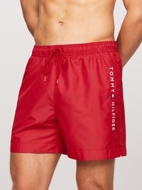 Røde badebukser med snoretræk i taljen, lavet af glat og let materiale, med hvid "TOMMY HILFIGER"-logo trykt vertikalt.