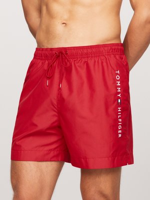 Pantaloncini da bagno rossi con vita regolabile tramite cordoncino, realizzati in materiale liscio e leggero, con il logo "TOMMY HILFIGER" stampato in verticale in bianco.