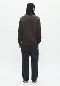 Bruine sweatshirt met geribde manchet en zoom, gecombineerd met donkerblauwe broek met zijzakken en beige schoeisel.