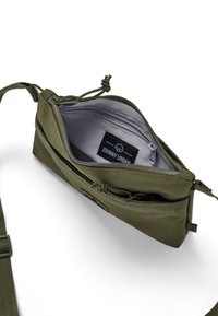 Borsa in tessuto verde oliva con scomparto con cerniera, interno grigio e tracolla regolabile. Presenta un'etichetta con marchio e particolare di chiusura con cordoncino.
