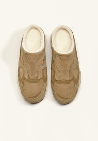 Beige ruskind slip-on sko med blød, hvid pelsforing; har en rundet tå og strukturerede detaljer.