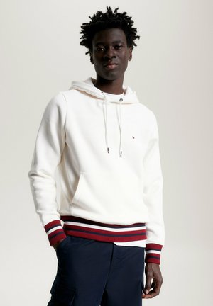 Weißer Hoodie mit einer Vordertasche, verstellbaren Kordeln und burgunderfarbenen, roten und blauen gestreiften Rippbündchen und Saum. Weiches Material.