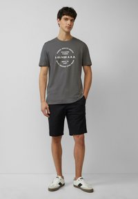 Grijze katoenen T-shirt met een cirkelvormige witte print, gecombineerd met zwarte shorts en witte sneakers met zwarte accenten. Eenvoudig, casual ontwerp.