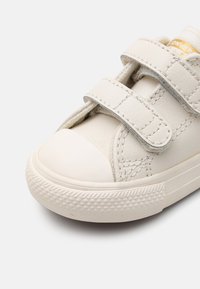 Hvite lær sneakers med borrelås, rund tåhette, teksturert gummisåle og synlige sømdetaljer.