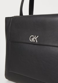 Borsa a mano in pelle nera con una texture liscia, forma strutturata, tasca frontale e un accento con logo "G&K" in argento.