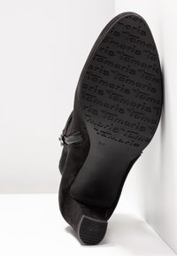 Zwarte suède enkellaars met een geribbelde rubberen zool, zijrits en een taps toelopende hak. Maat 37 is in de zool geperst.