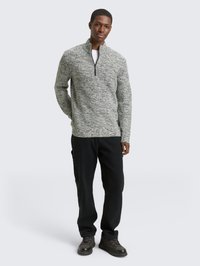 Grijs en zwart textuur patroon sweater met kwart rits, gemaakt van een gebreide stof, gecombineerd met zwarte broek en donkere schoenen.