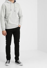 Felpa grigia con cappuccio e lacci, con tasca frontale, abbinata a jeans neri e sneaker neri. Design semplice, in tessuto di cotone, vestibilità casual.