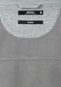 Pull-over en polaire gris avec un col rond, étiquette grise contrastante portant les mentions "INDIGO" et "MEDIUM", et surface en tissu texturé.