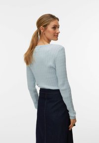 Pull côtelé bleu clair à manches longues et col rond, associé à une jupe en jean foncé, vu de dos.